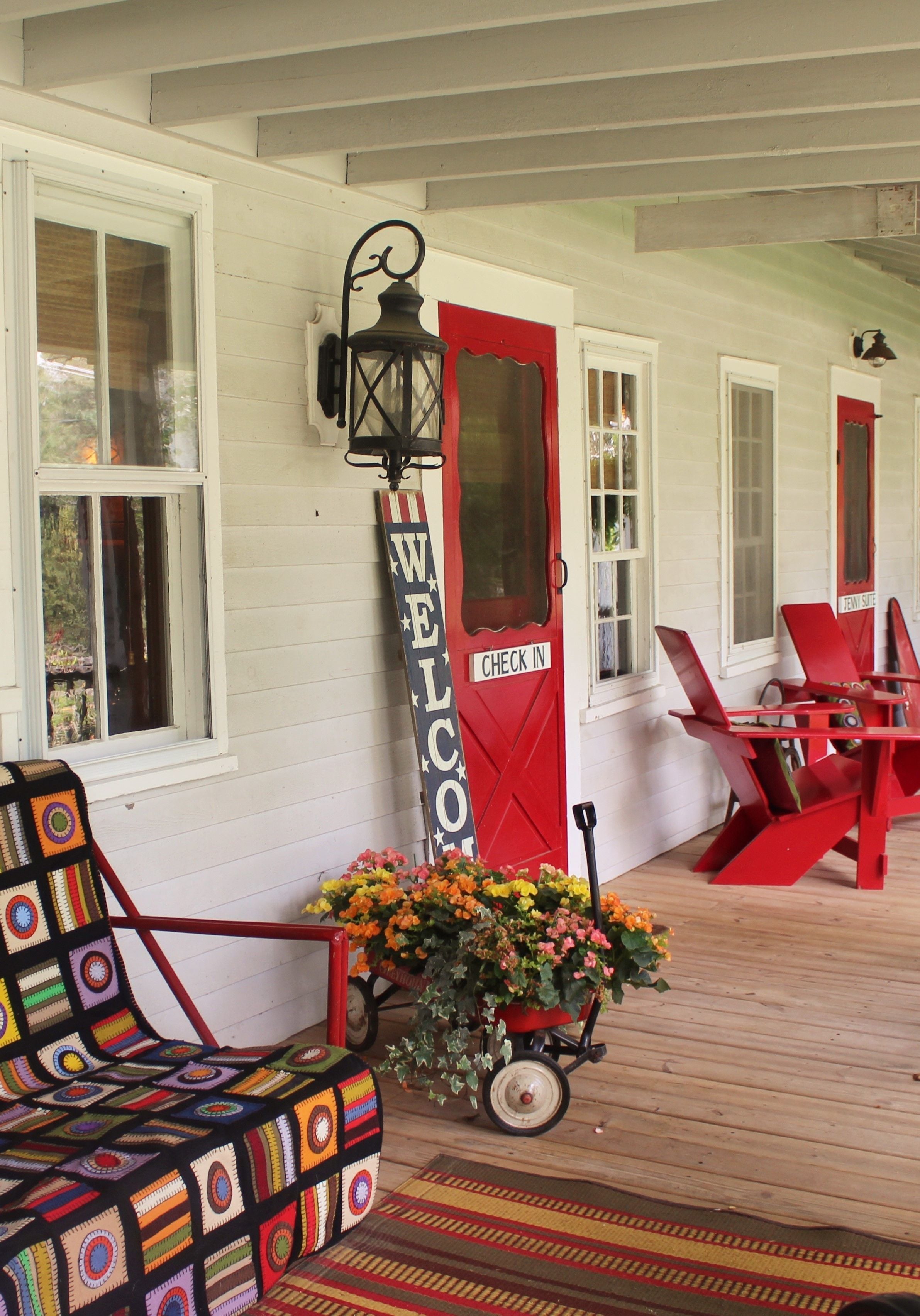A porch with a red chair, a welcome sign, and a flower cart.