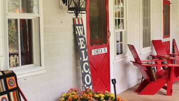 A porch with a red chair, a welcome sign, and a flower cart.