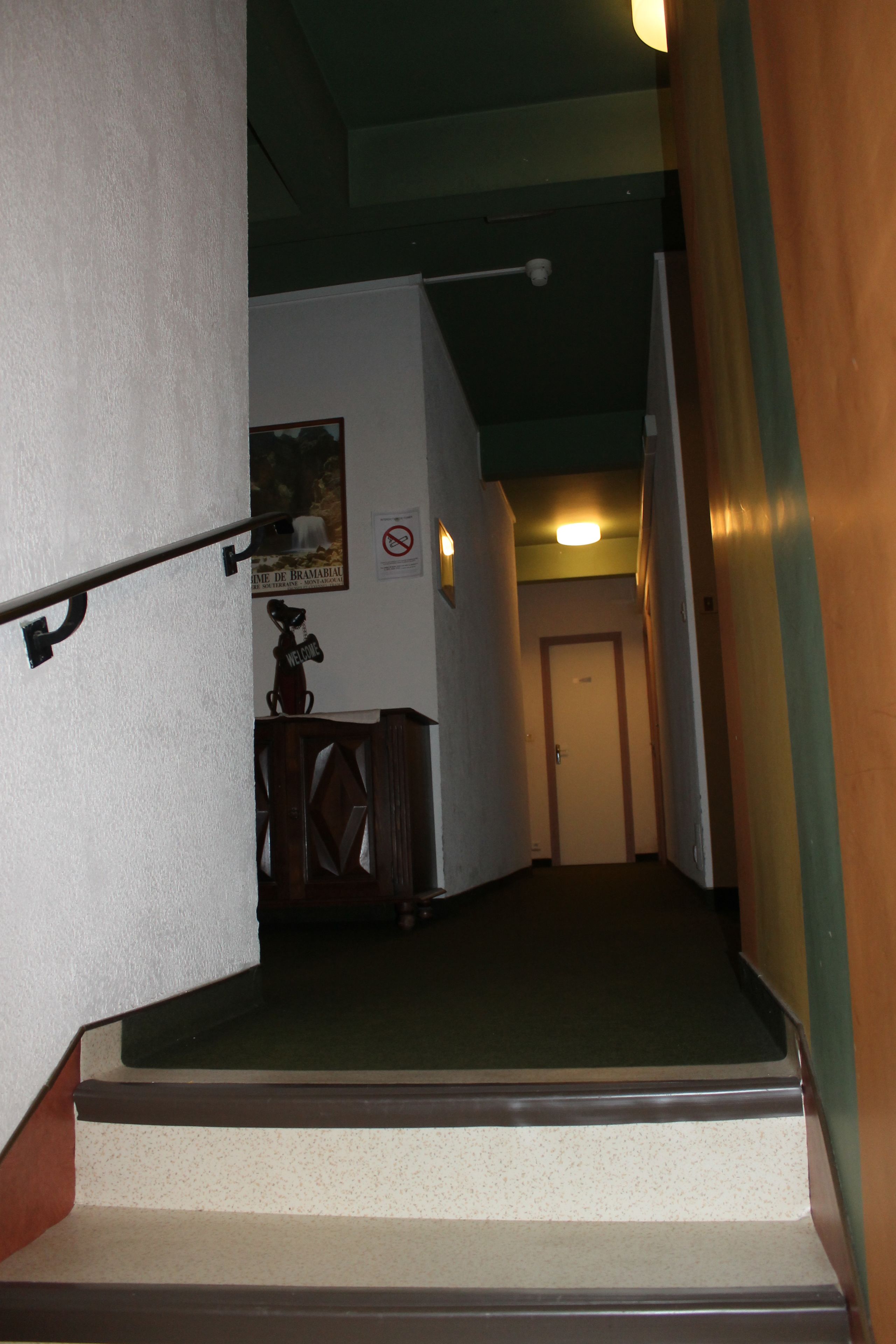 Un couloir étroit avec un escalier menant à une porte au fond.