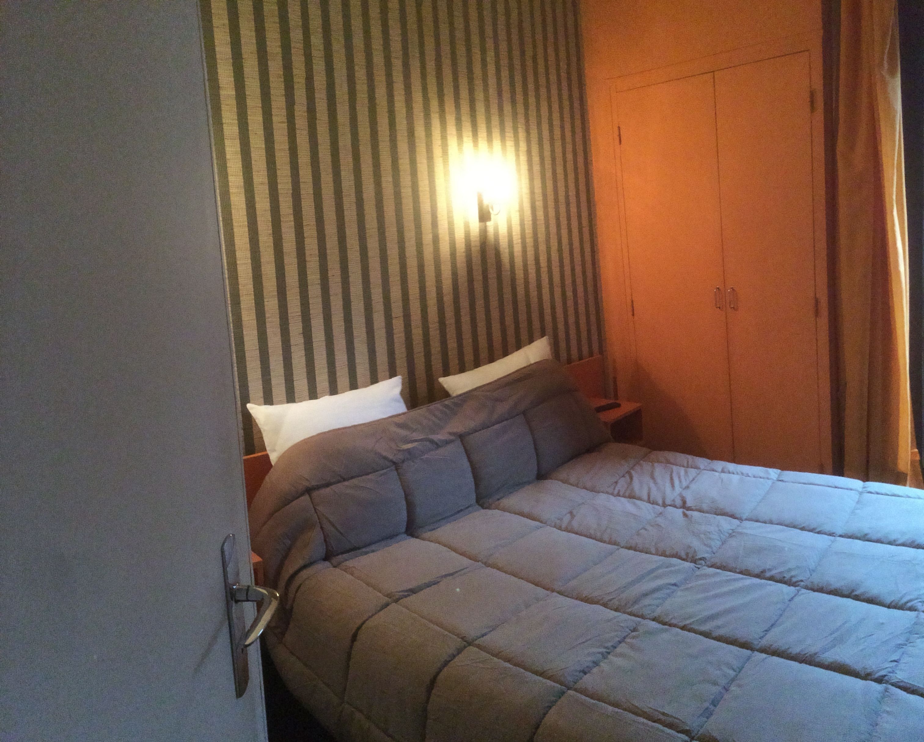 Una camera d'albergo con un letto, una testiera a righe e un armadio.