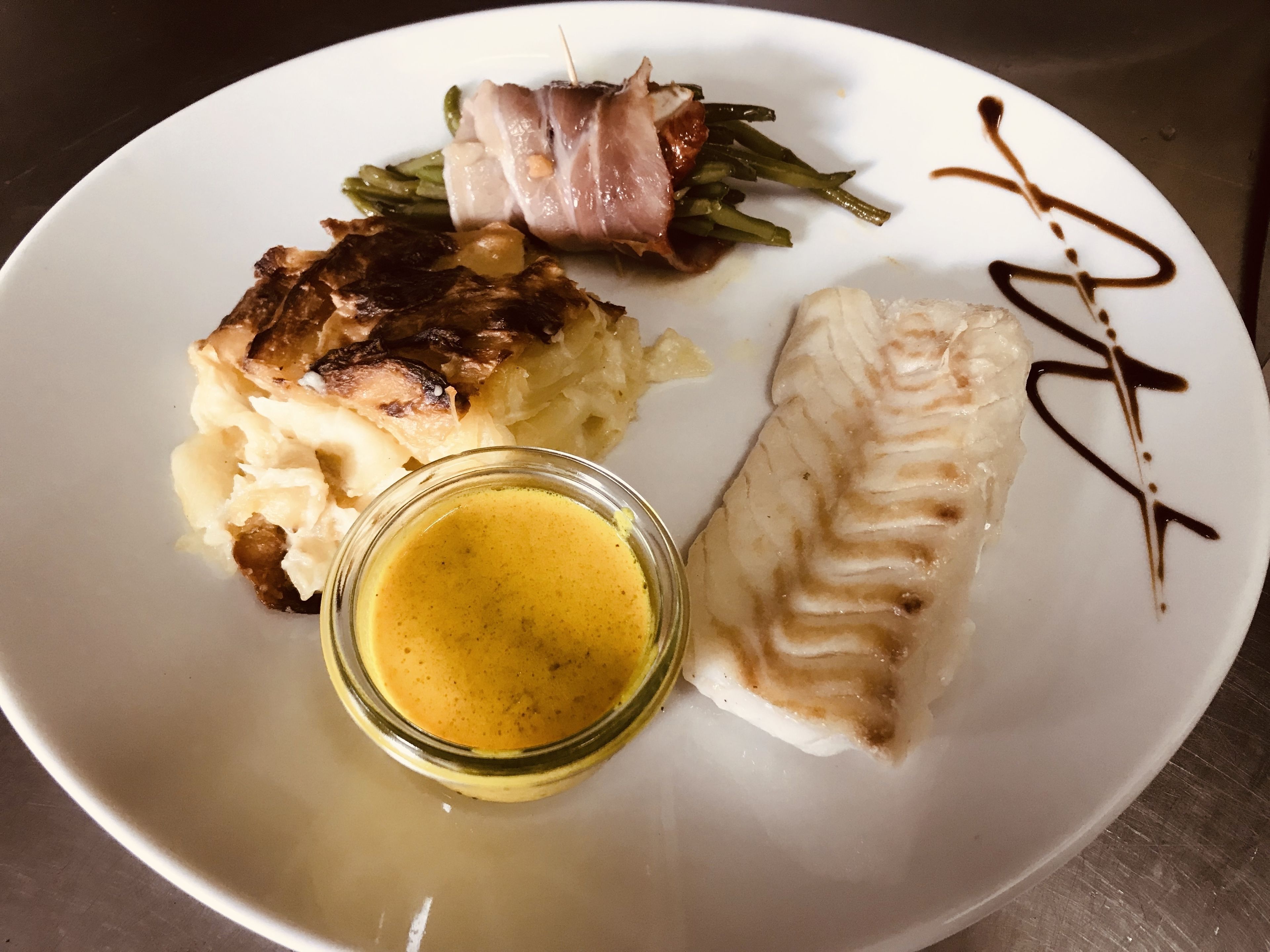 A plate with various food items including fish, potatoes, and greens, accompanied by a small bowl of sauce.