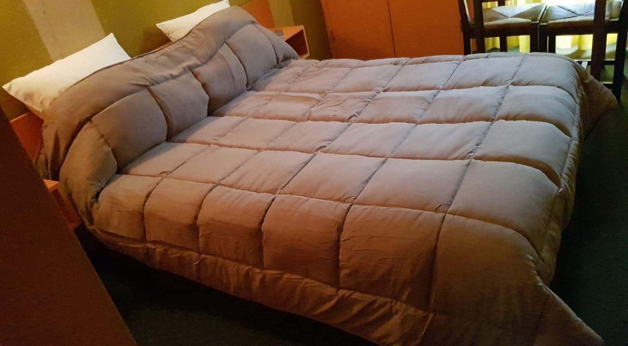 A bed with a beige quilted duvet, two white pillows, and a wooden headboard.