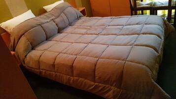 A bed with a beige quilted duvet, two white pillows, and a wooden headboard.
