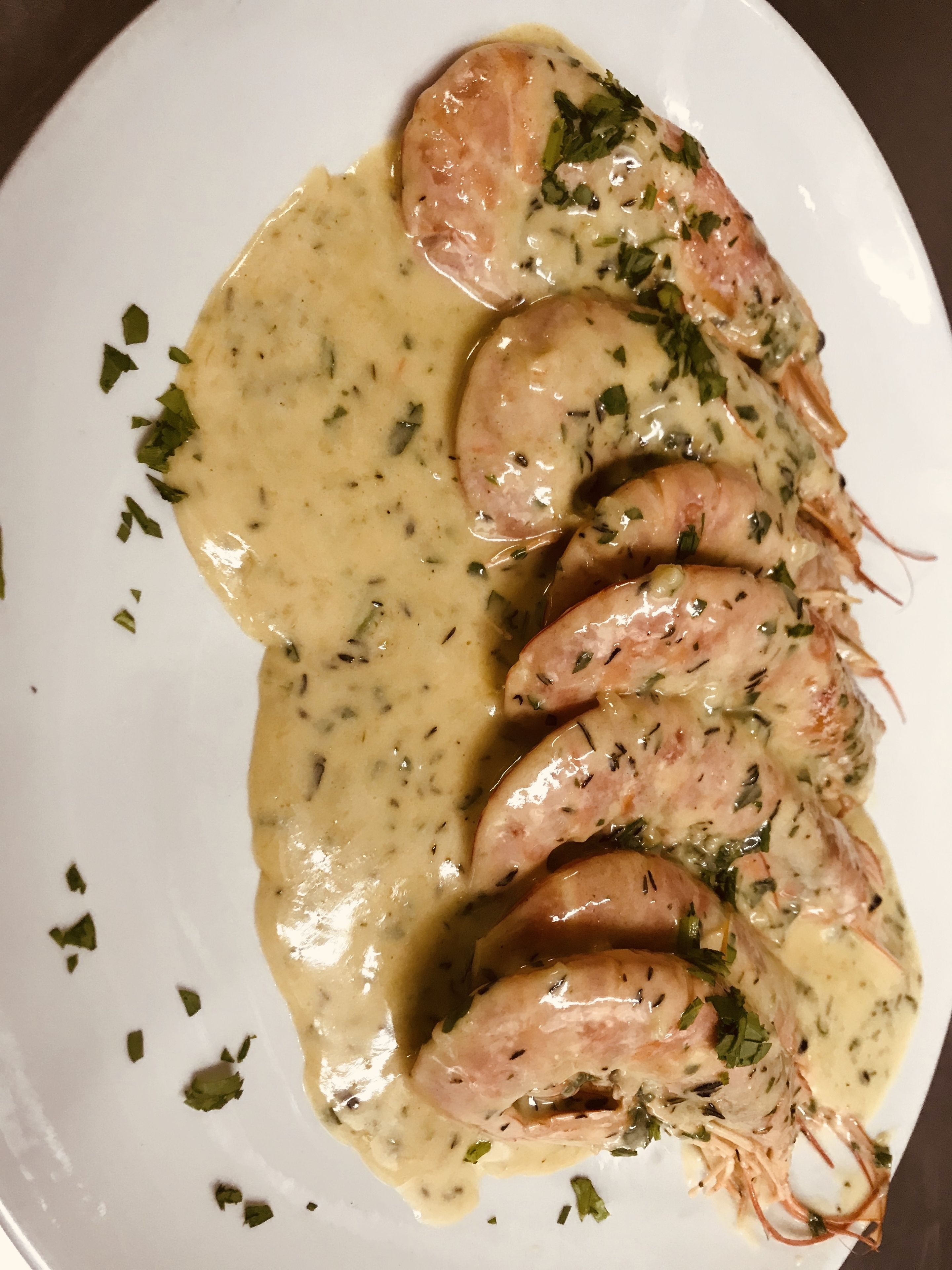 A plate of shrimp with a creamy sauce and herbs.