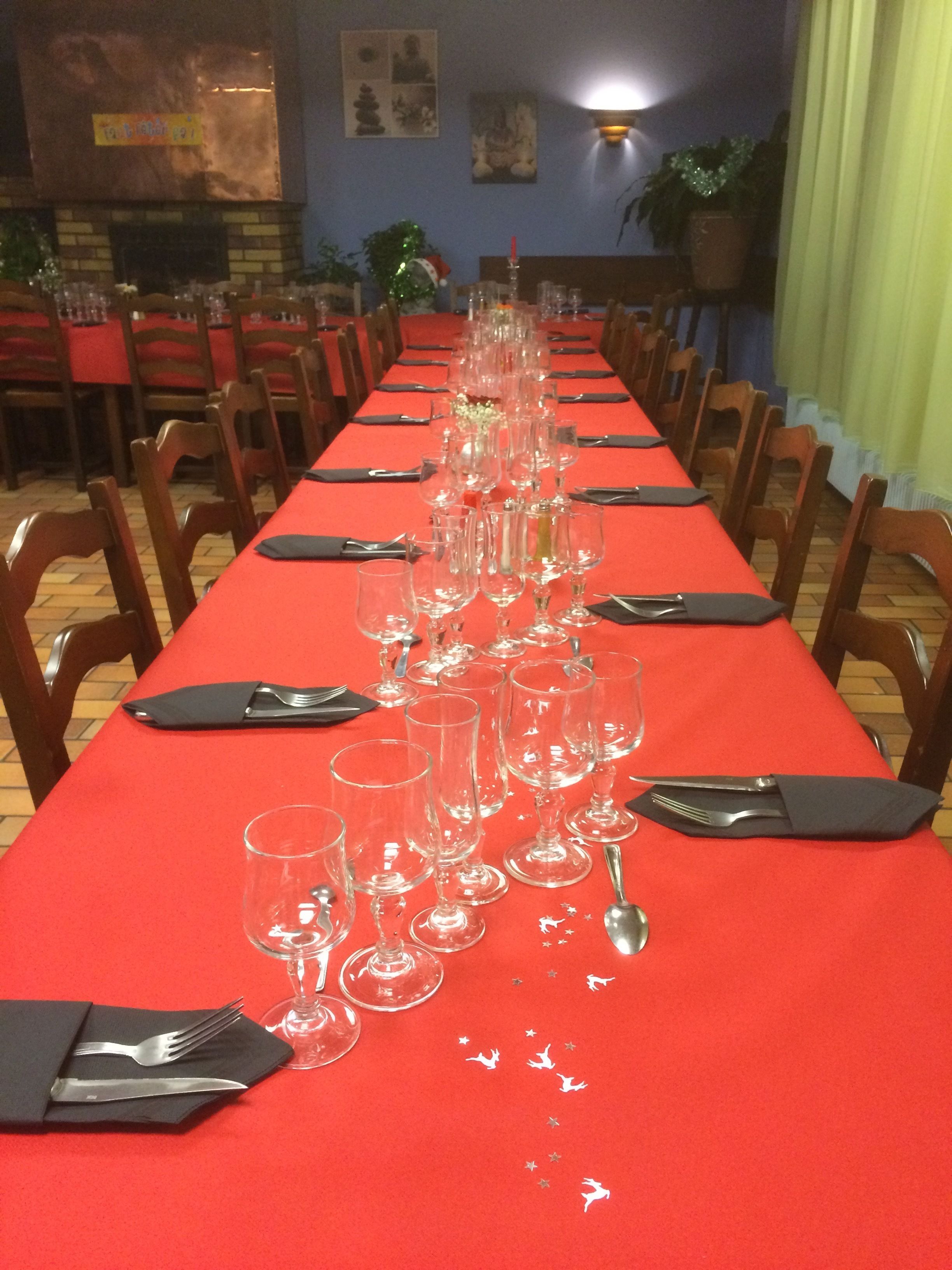 A long dining table with a red tablecloth, set with multiple wine glasses, forks, and spoons.