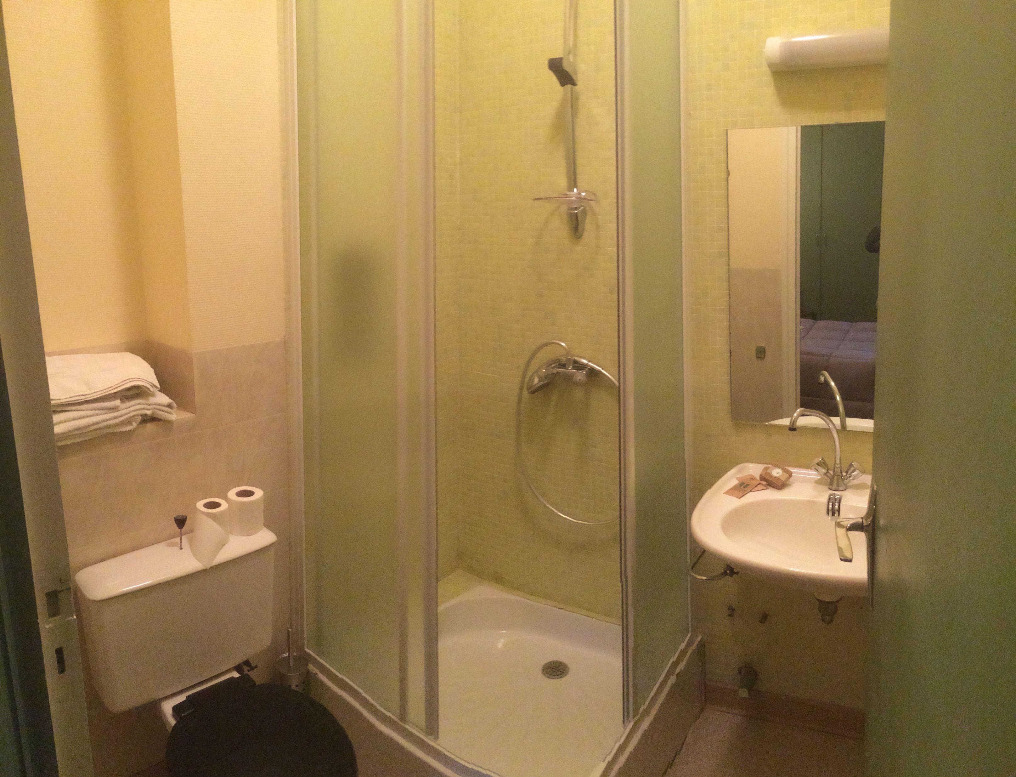 A small bathroom with a shower, toilet, sink, and a stack of white towels.