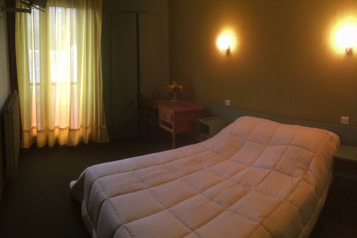 A hotel room with a bed, a nightstand, a desk, and a window with curtains.
