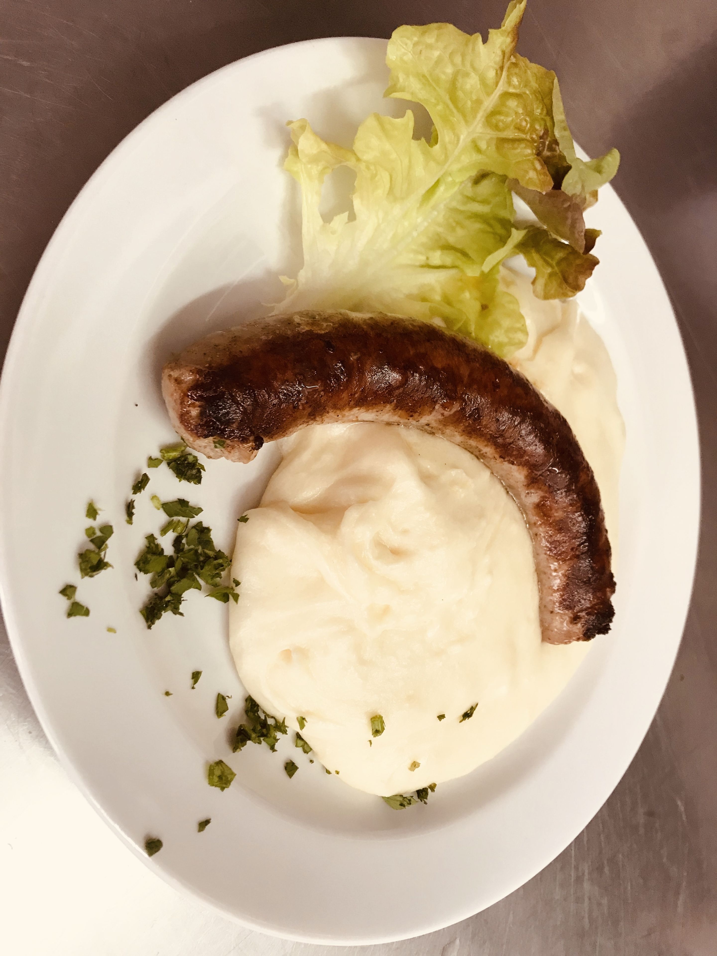 Un plato con salchicha, puré de papas y lechuga.