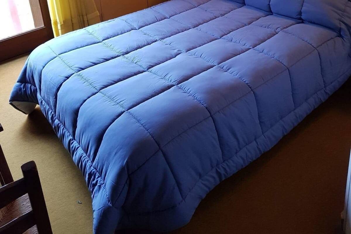 A bedroom with a blue bedspread, a wardrobe, a nightstand, and a wall-mounted light.