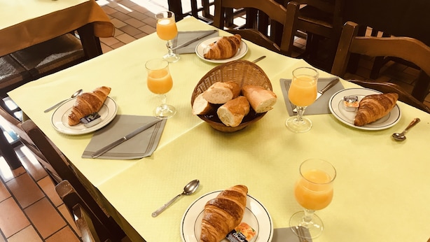 A breakfast setting with croissants, orange juice, and a basket of bread on a table. - L'Agapanthe (Pont-de-Salars)