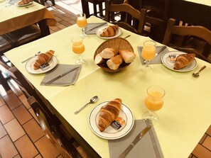 A breakfast setting with croissants, orange juice, and a basket of bread on a table. - L'Agapanthe (Pont-de-Salars)