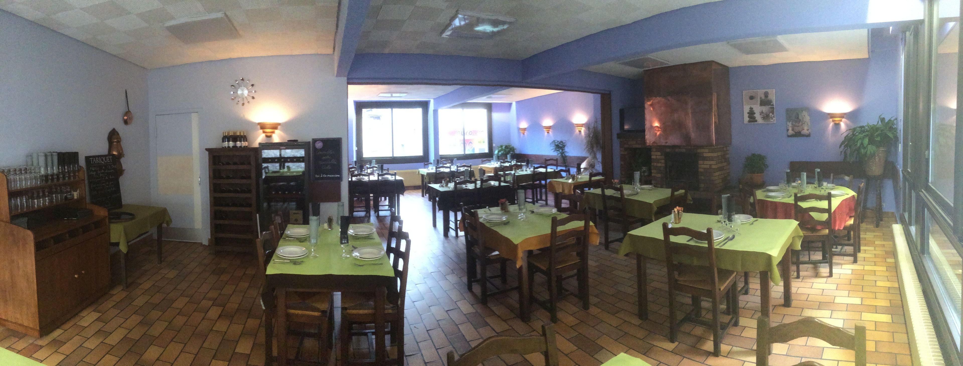 A restaurant with multiple dining tables, chairs, a brick floor, and a fireplace.