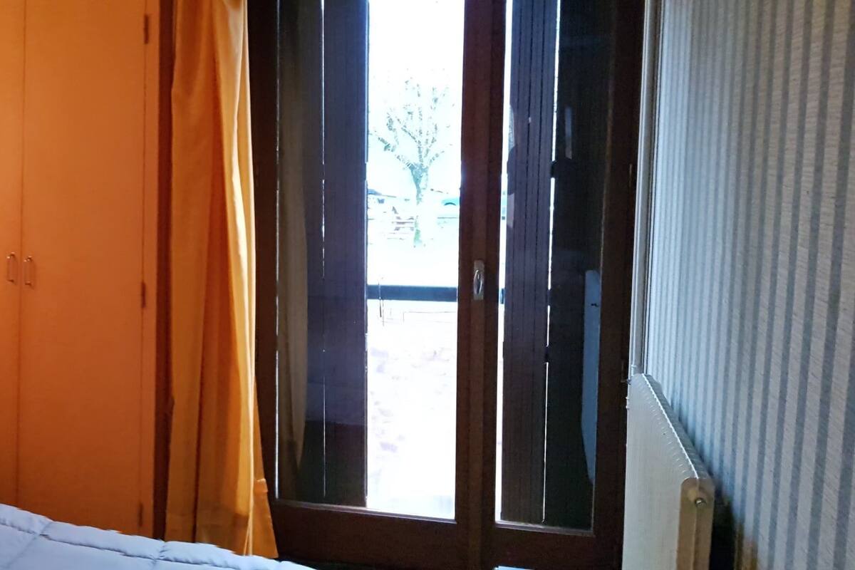 A room with a bed, a nightstand, a wall-mounted light, and a window with curtains.