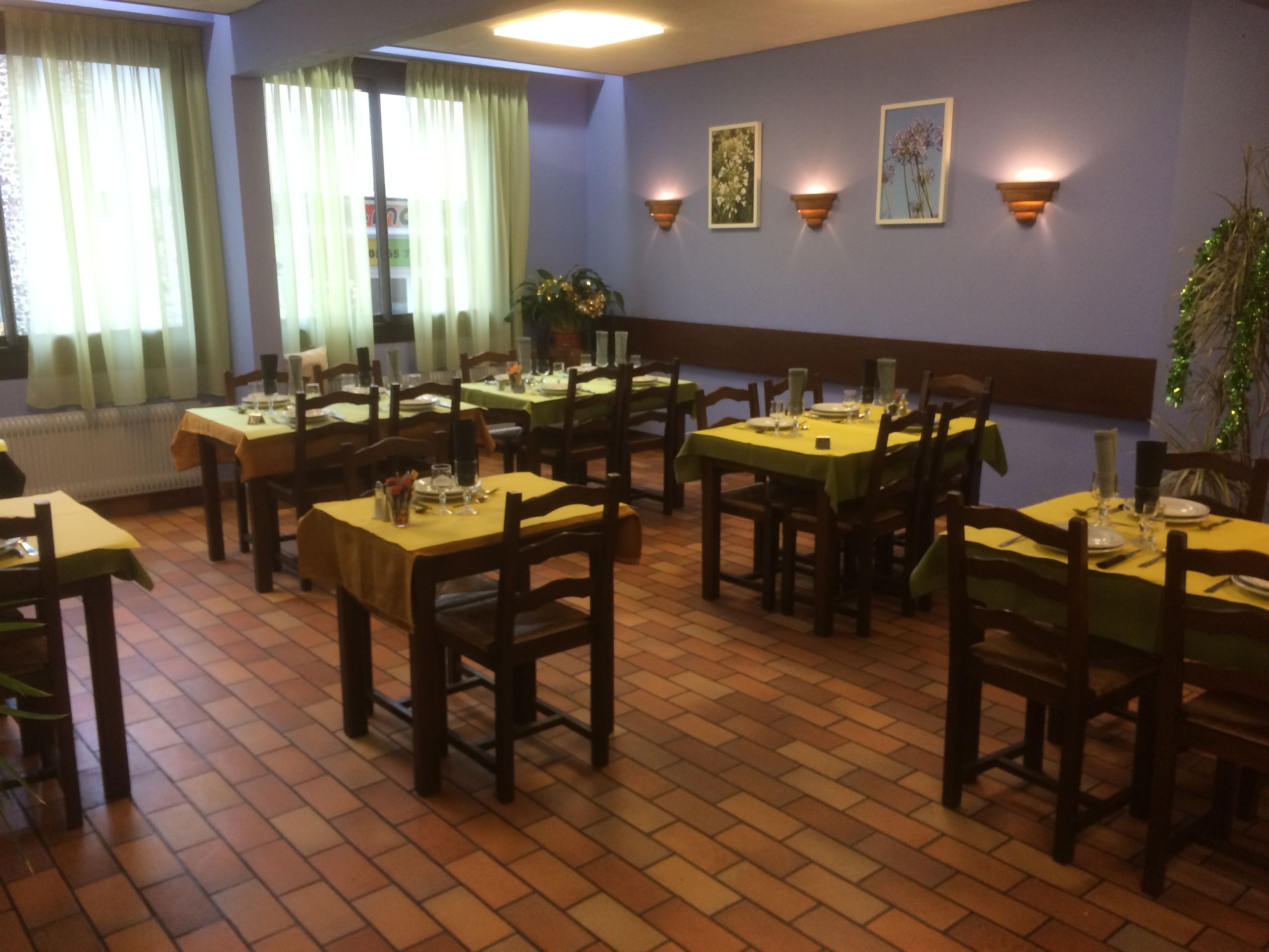 A restaurant with multiple tables and chairs, green tablecloths, and wall-mounted light fixtures.