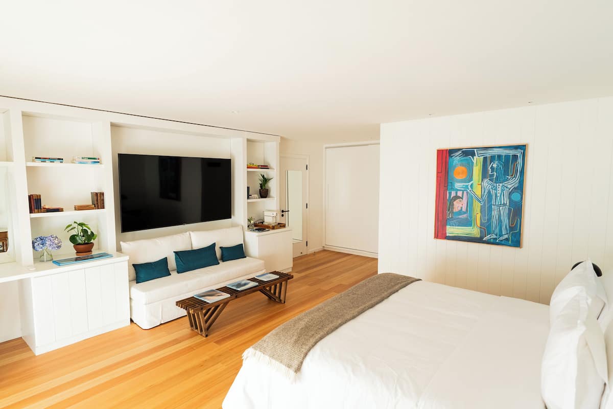 A modern hotel room with a large bed, a sofa, a TV, and a painting on the wall.