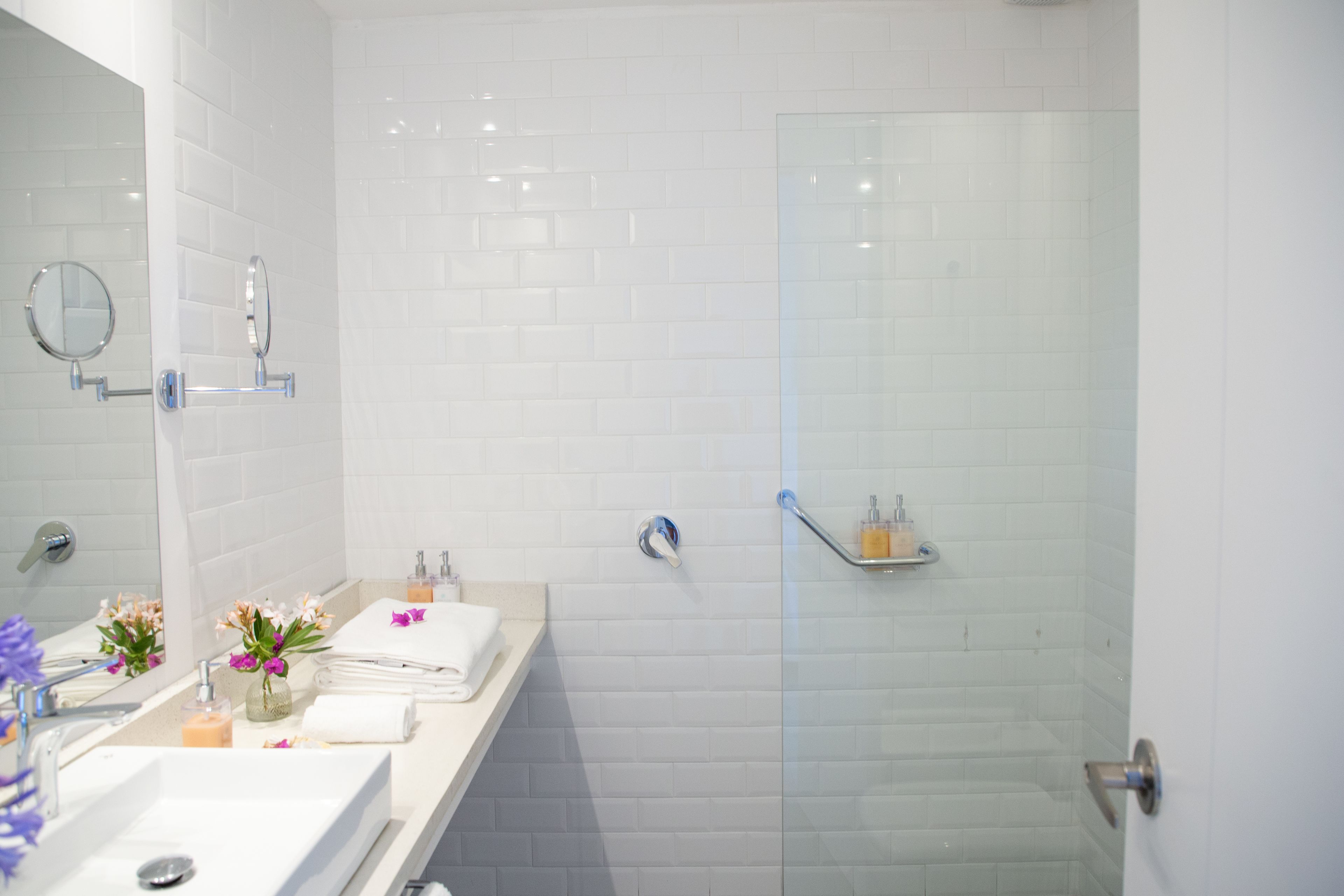 A modern bathroom with white tiled walls, a glass shower enclosure, a vanity with a mirror, and a towel rack.