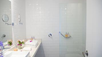 A modern bathroom with white tiled walls, a glass shower enclosure, a vanity with a mirror, and a towel rack.