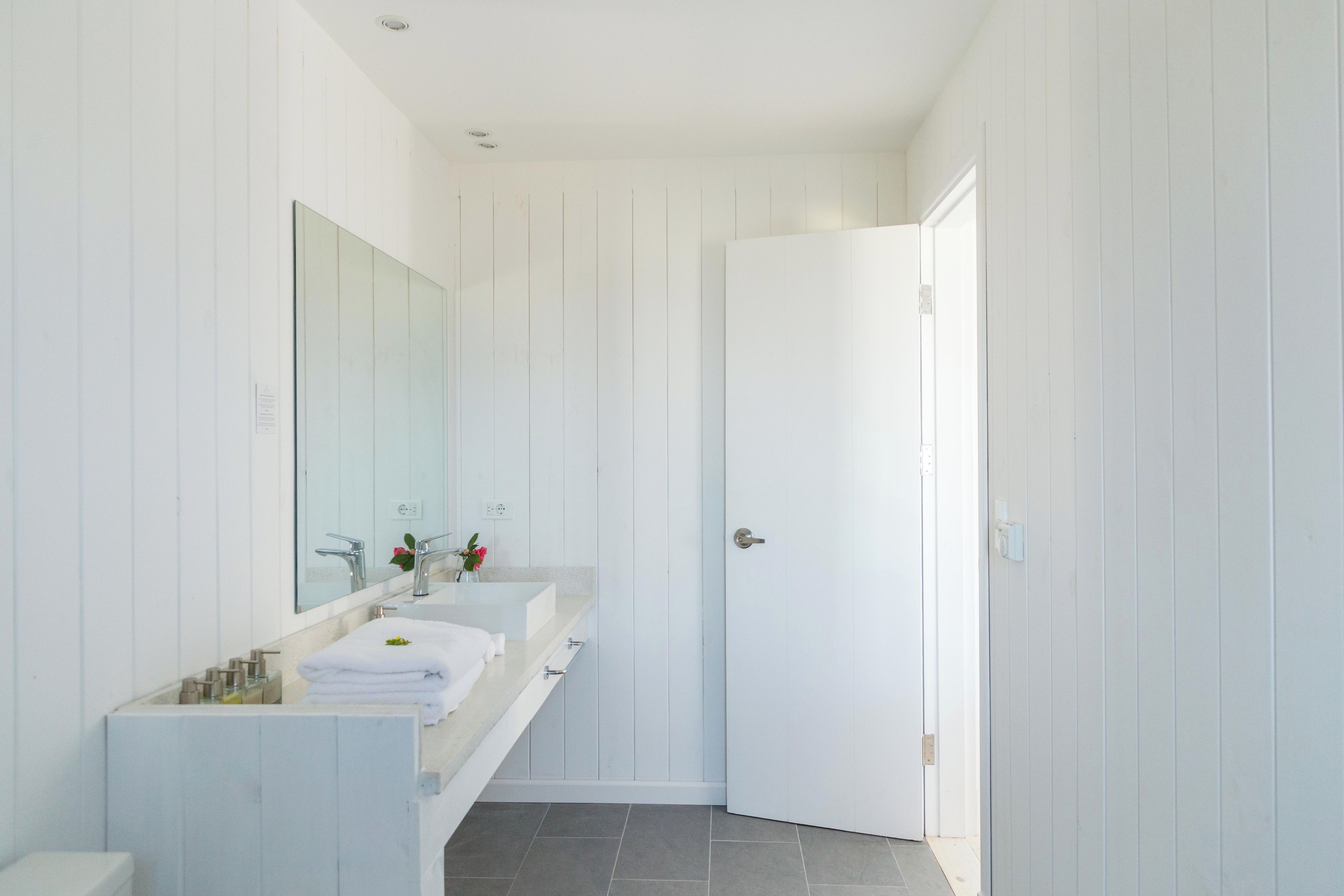 Un baño moderno con tocador blanco, un espejo grande y una puerta que da a otra habitación.
