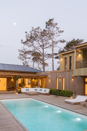 Una casa moderna con piscina, fachada de madera y balcón con mobiliario de exterior.