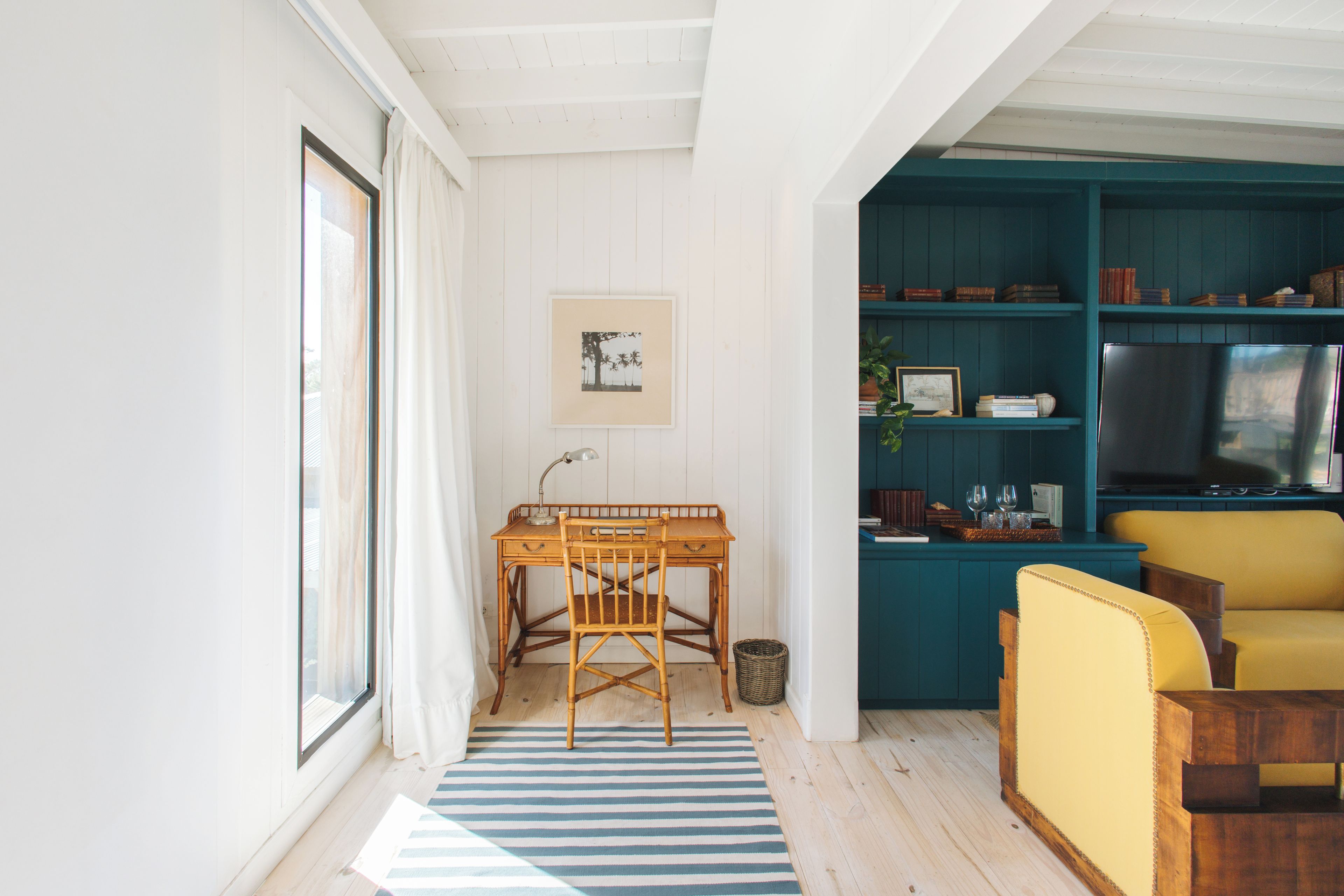Una habitación con un escritorio de madera, una silla, un alfombra a rayas, una estantería y un televisor.