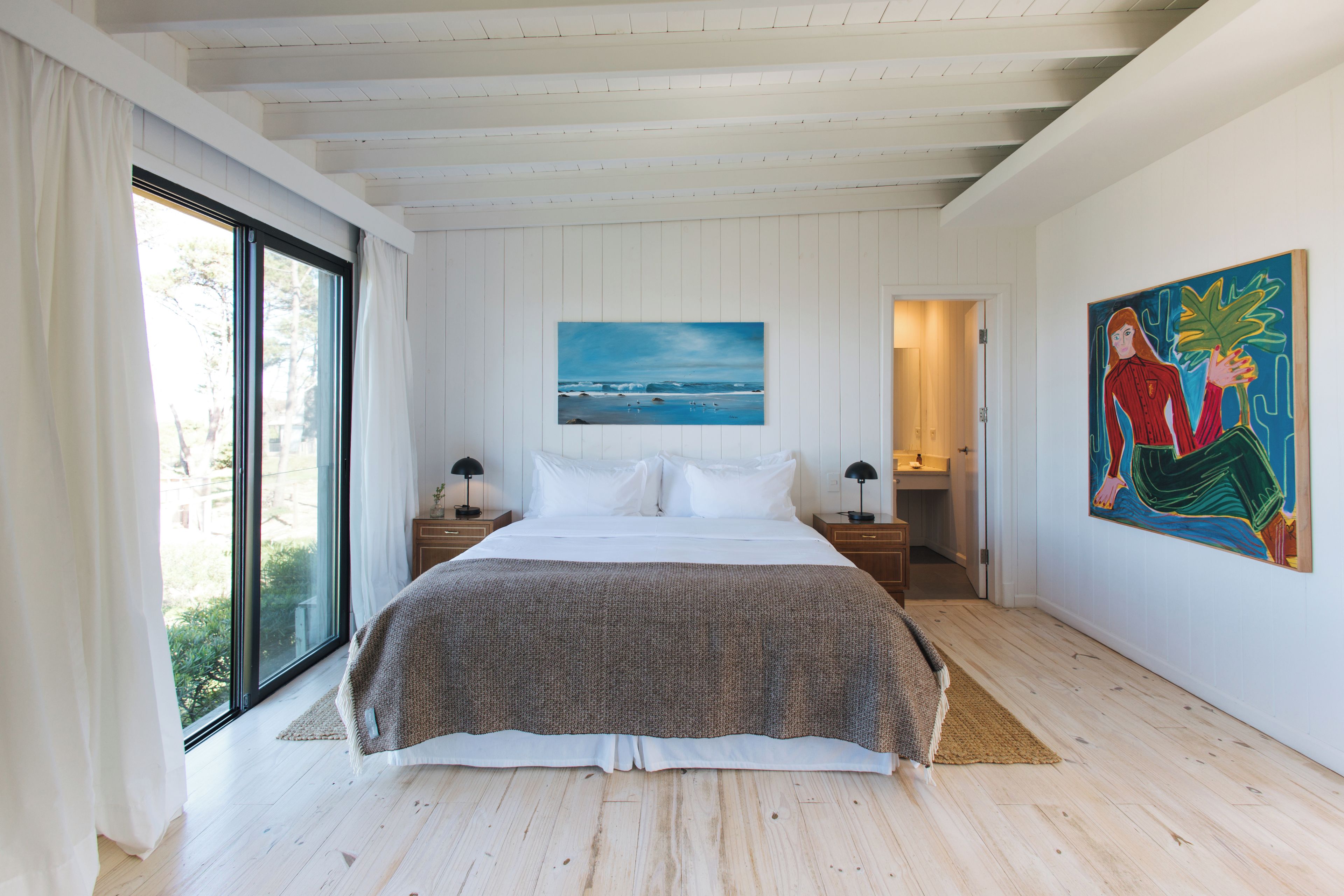 Ein Schlafzimmer mit einem großen Bett, einem Gemälde an der Wand und Blick durch ein Fenster.