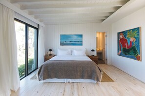 A bedroom with a large bed, a painting on the wall, and a view through a window. - Casa Flor - Adults Only (Punta del Este)