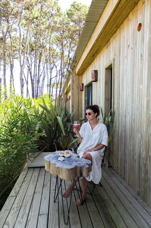 A person seated at a wooden table on a deck with a wooden building in the background. - Casa Flor - Adults Only (Punta del Este)