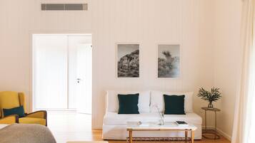 A living room with a white sofa, two green cushions, a coffee table, a yellow armchair, and a small side table with a plant.