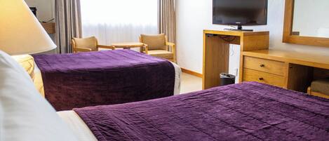 A hotel room with two beds, a desk with a television, a chair, and a lamp.