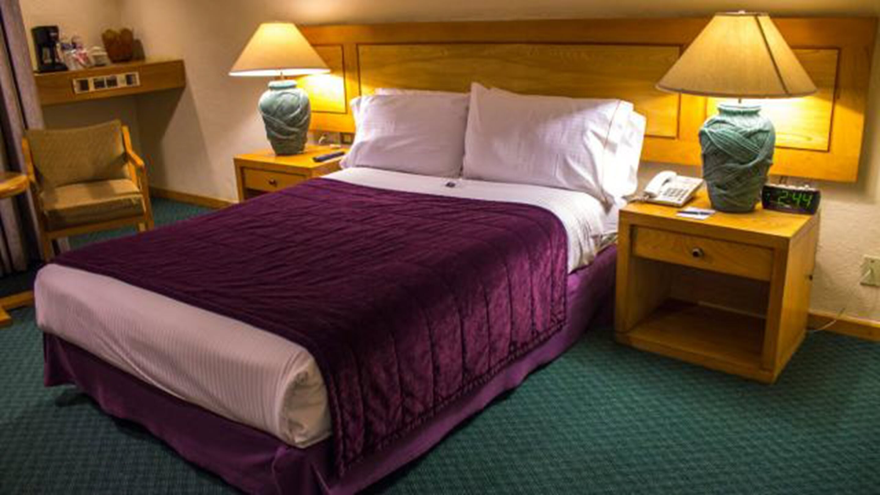 Una habitación de hotel con una cama, dos mesitas de noche, una silla y una lámpara en cada mesita.