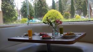 Ein Frühstückstisch mit Tellern voller Speisen, einer Blumenvase und einem Glas Orangensaft.