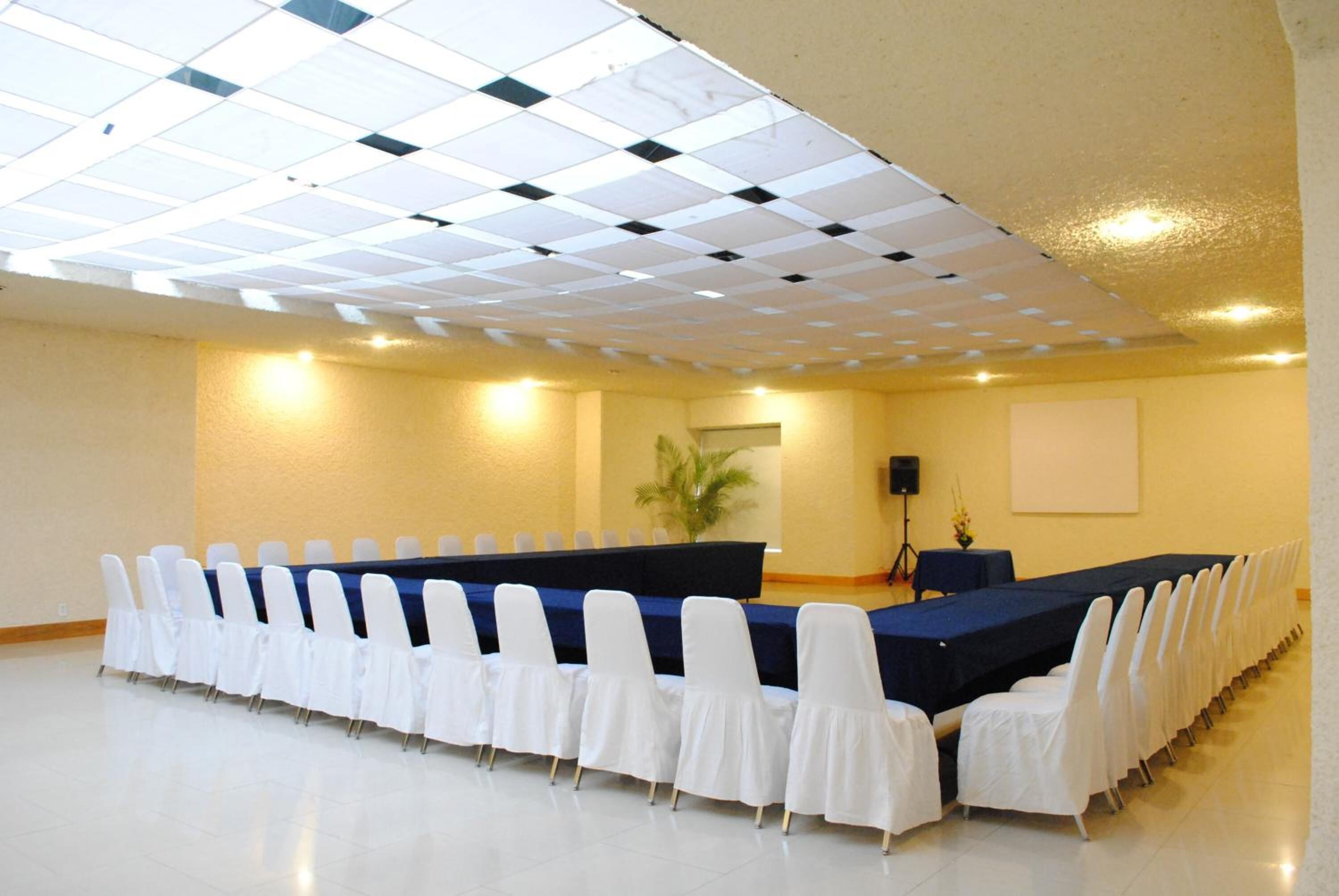 A conference room with a long table and white chairs, a projector screen, and a ceiling with a grid pattern.