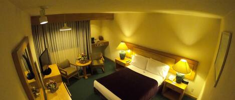 A hotel room with a bed, bedside tables, a desk, a chair, a lamp, and a mirror.