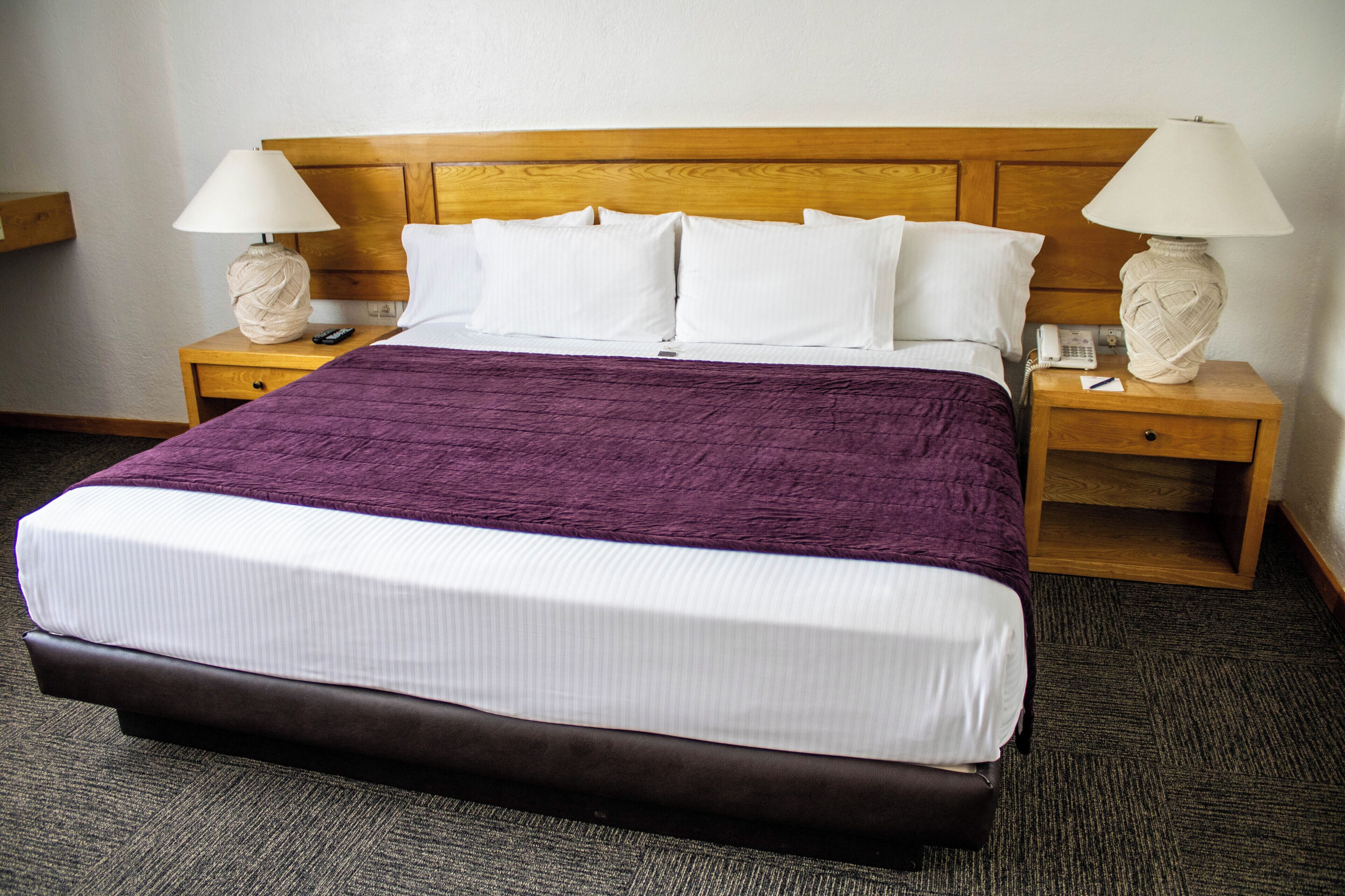 A hotel room with a large bed, two bedside tables with lamps, a telephone, and a small shelf.