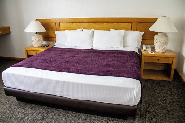 A hotel room with a large bed, two bedside tables with lamps, a telephone, and a small shelf.