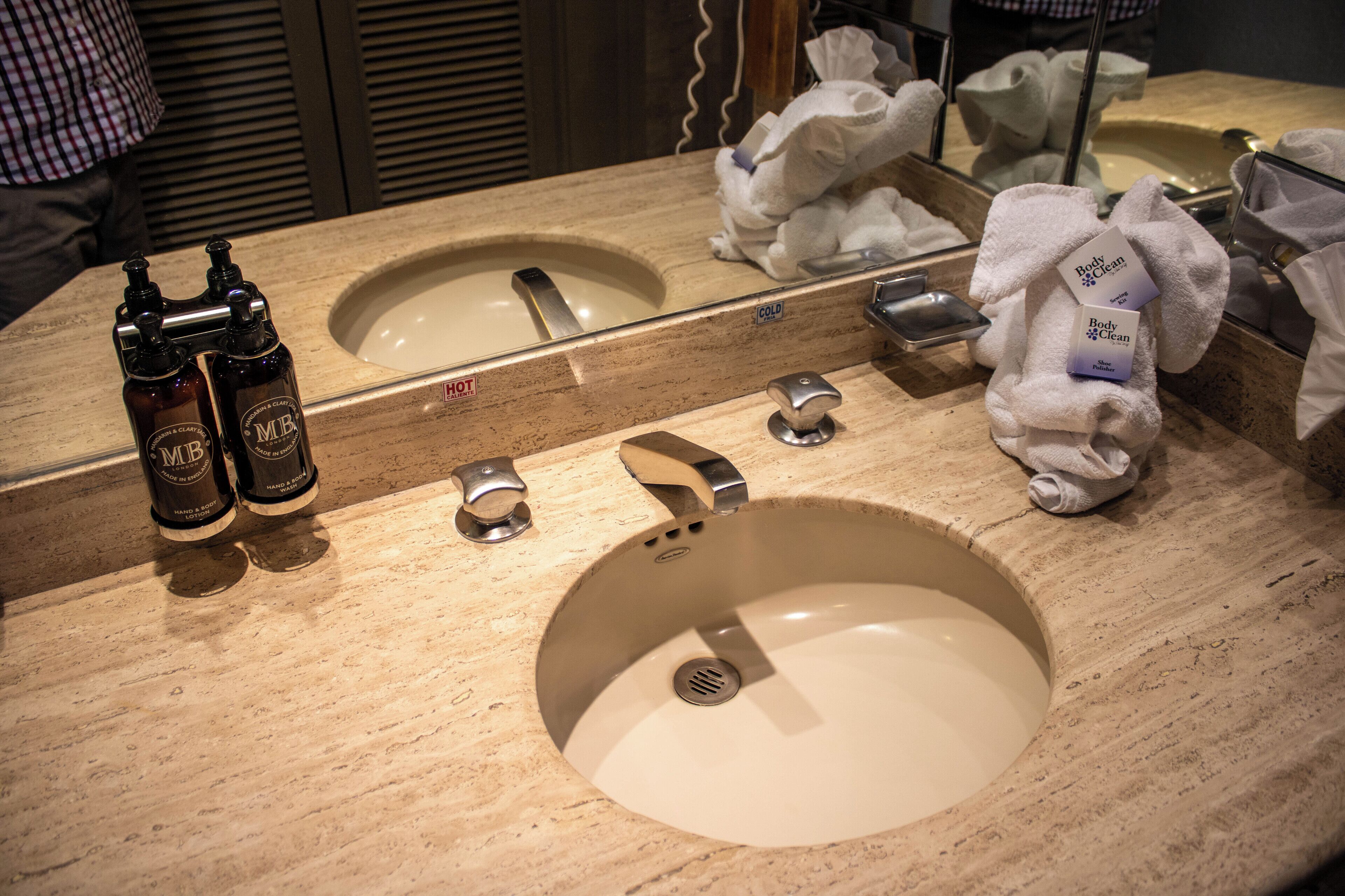 A bathroom sink with a mirror, two bottles of hand soap, a soap dispenser, and a towel dispenser.