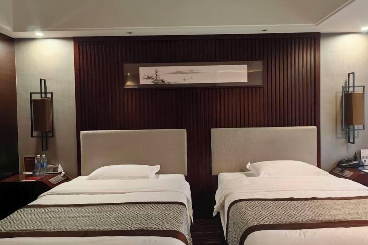 A hotel room with two beds, a wooden panel wall, and a painting above the beds.