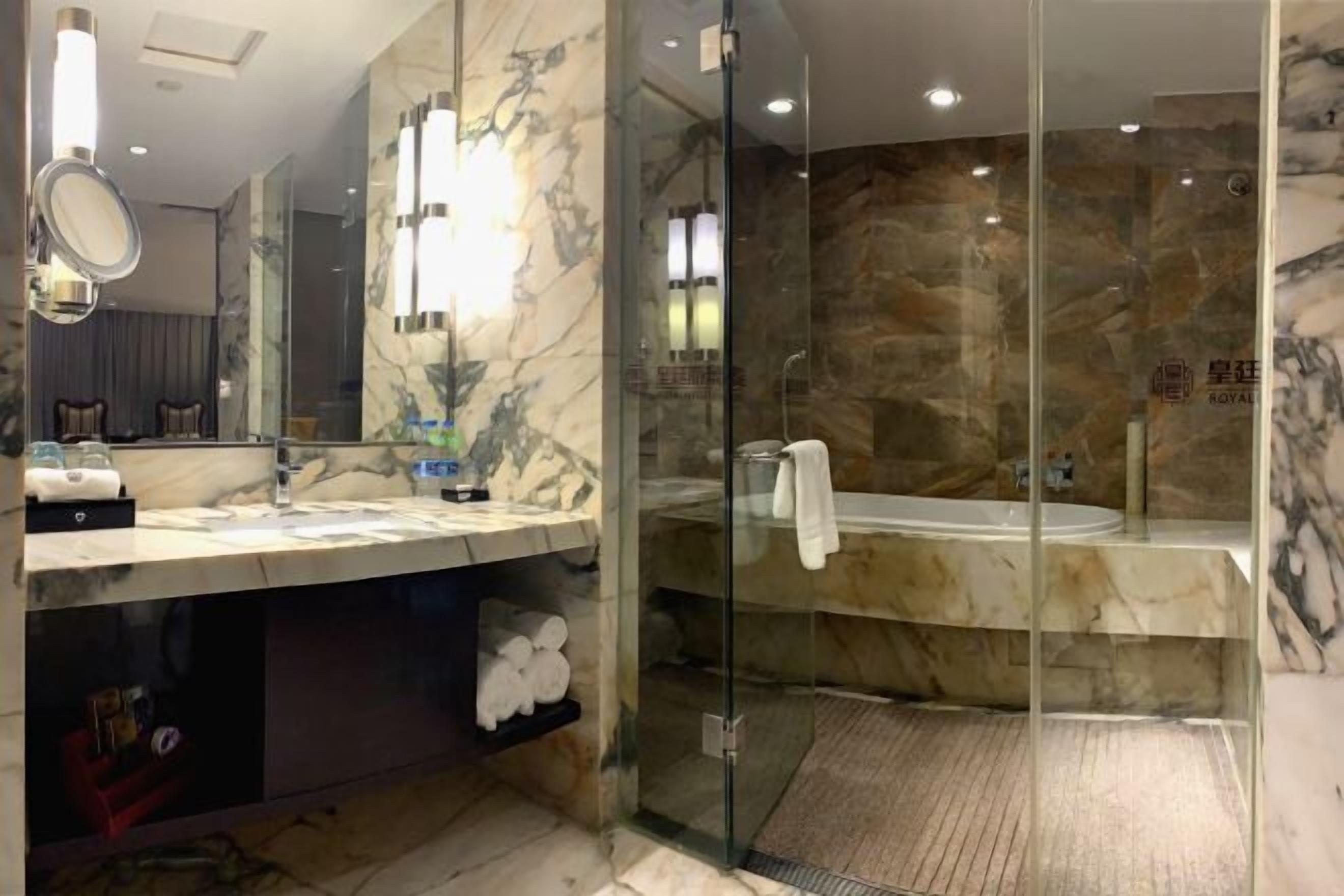 A modern bathroom with a glass-enclosed shower, marble countertops, and a large mirror.