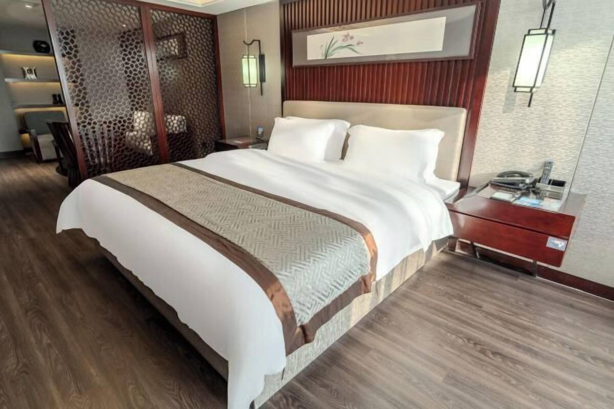 A hotel room with a large bed, a wooden headboard, a nightstand, and a decorative wall panel.