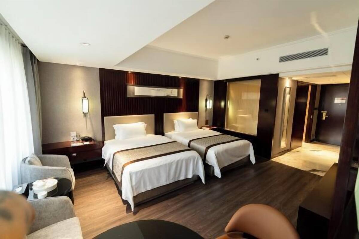 A hotel room with two beds, a desk, a chair, and a large mirror.