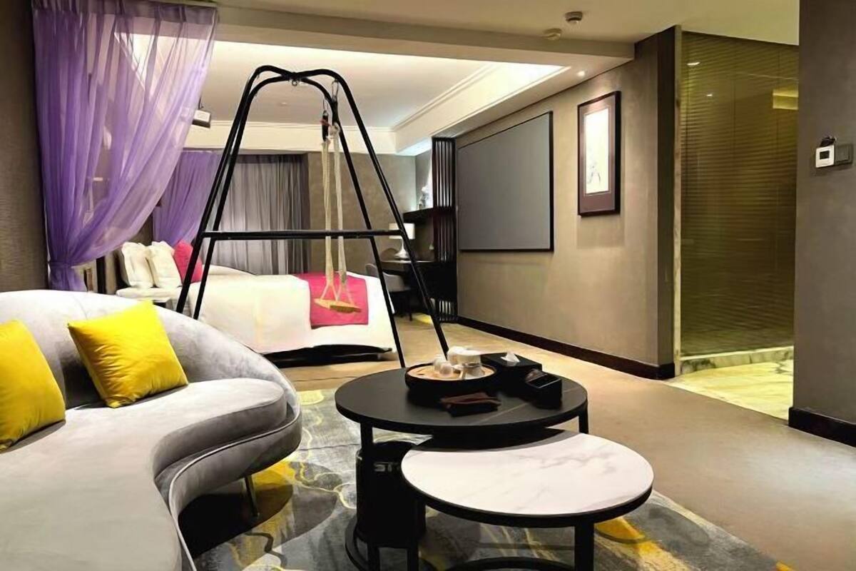 A modern hotel room with a bed, a sofa, a small table, and a swing chair.