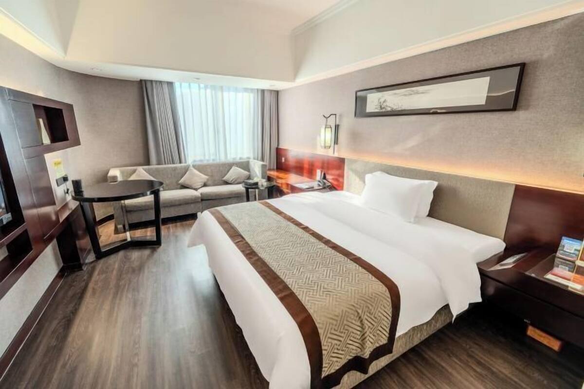 A hotel room with a large bed, a sofa, a desk, and a TV.