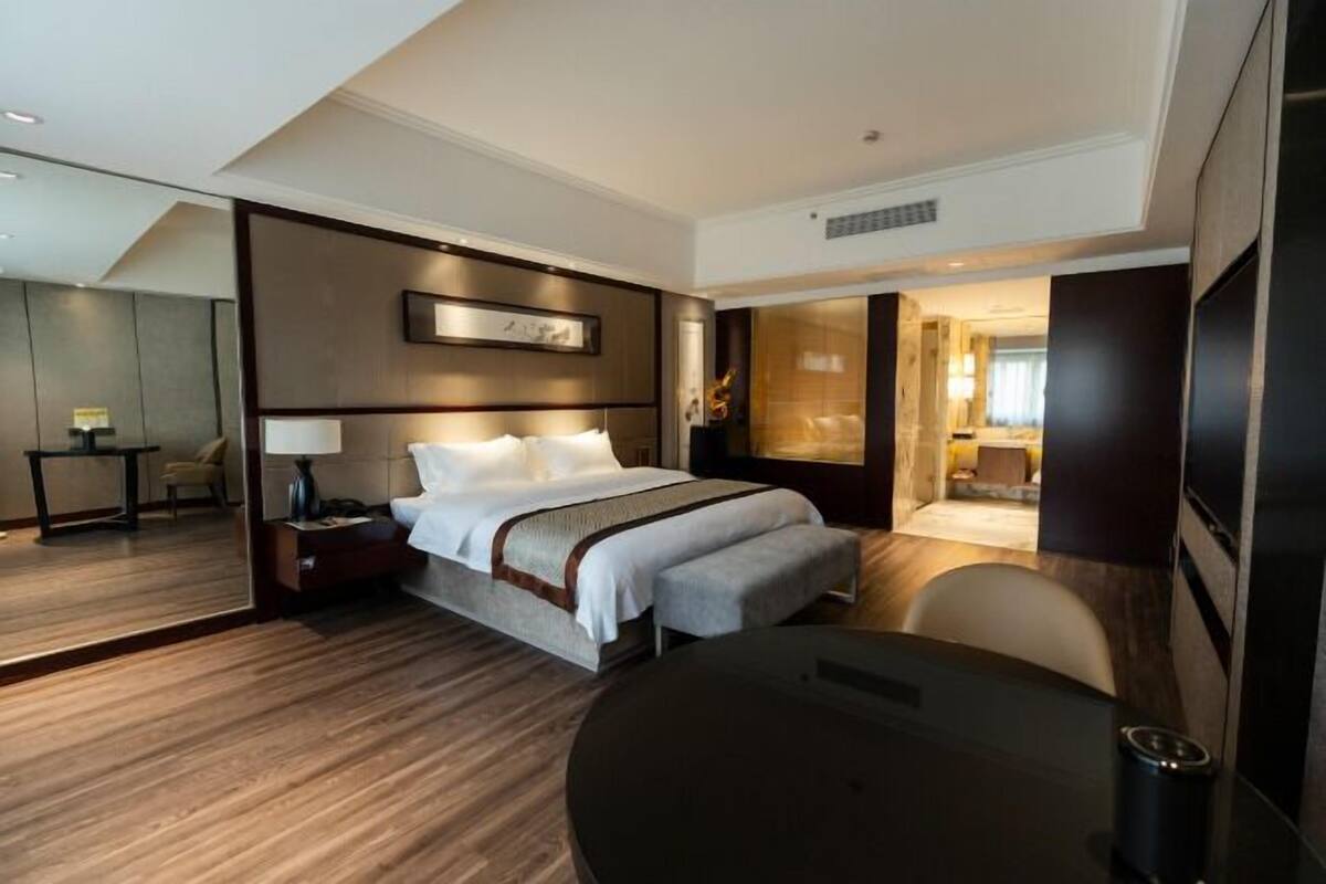 A modern hotel room with a large bed, a bedside table, a chair, and a desk.