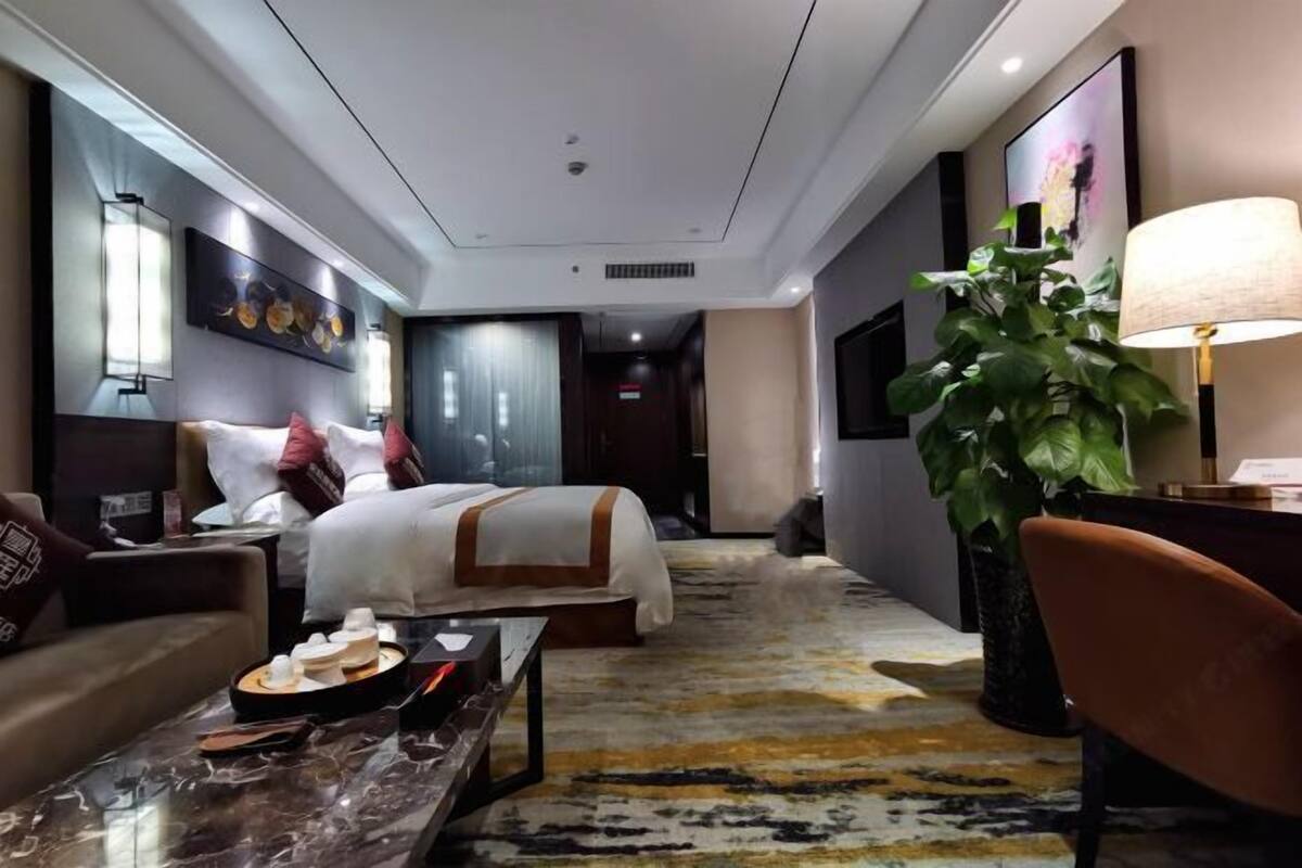 A hotel room with a bed, a sitting area with a table and chairs, a large potted plant, and artwork on the walls.