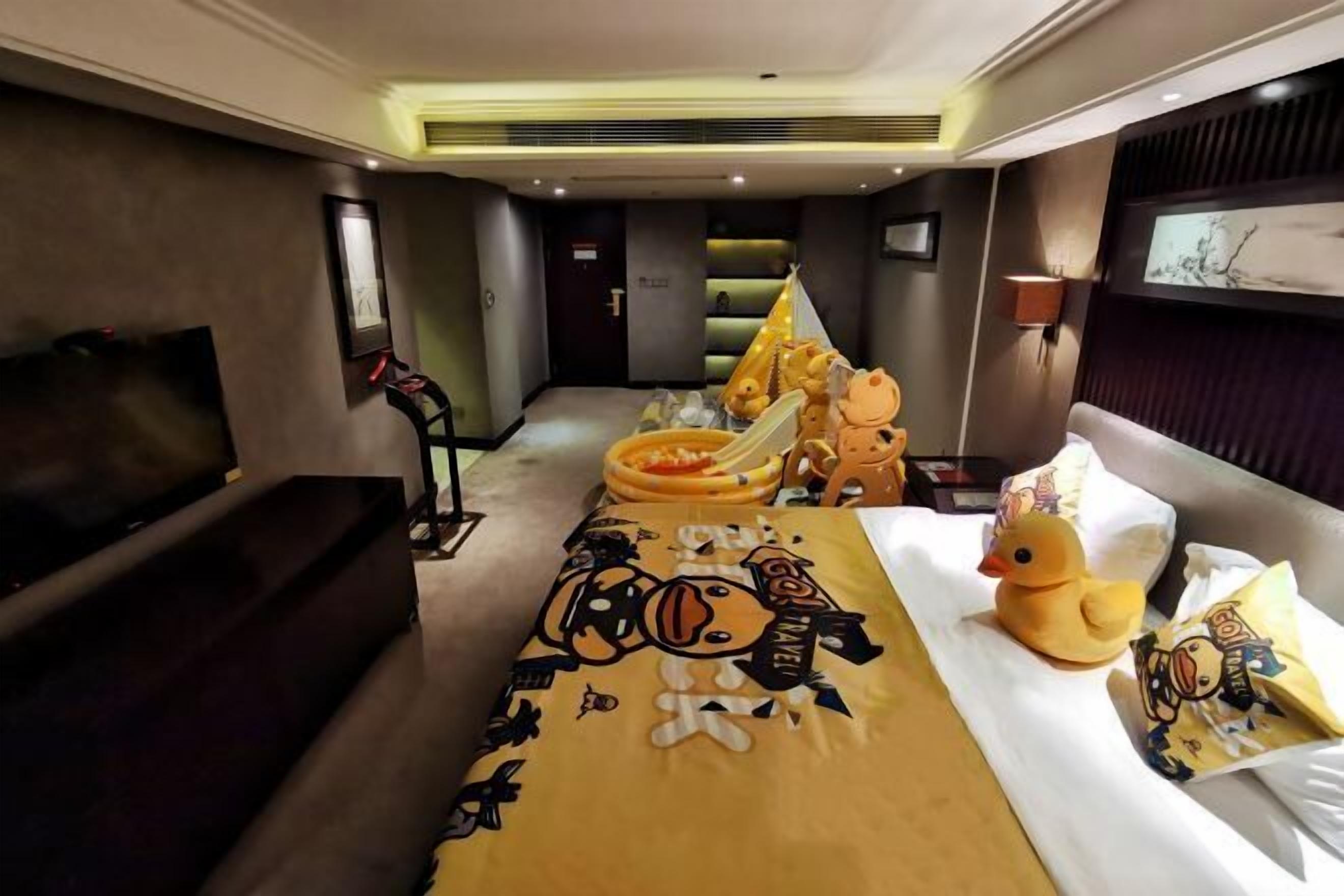 A hotel room with a bed, a sofa, a television, and a wall-mounted screen.