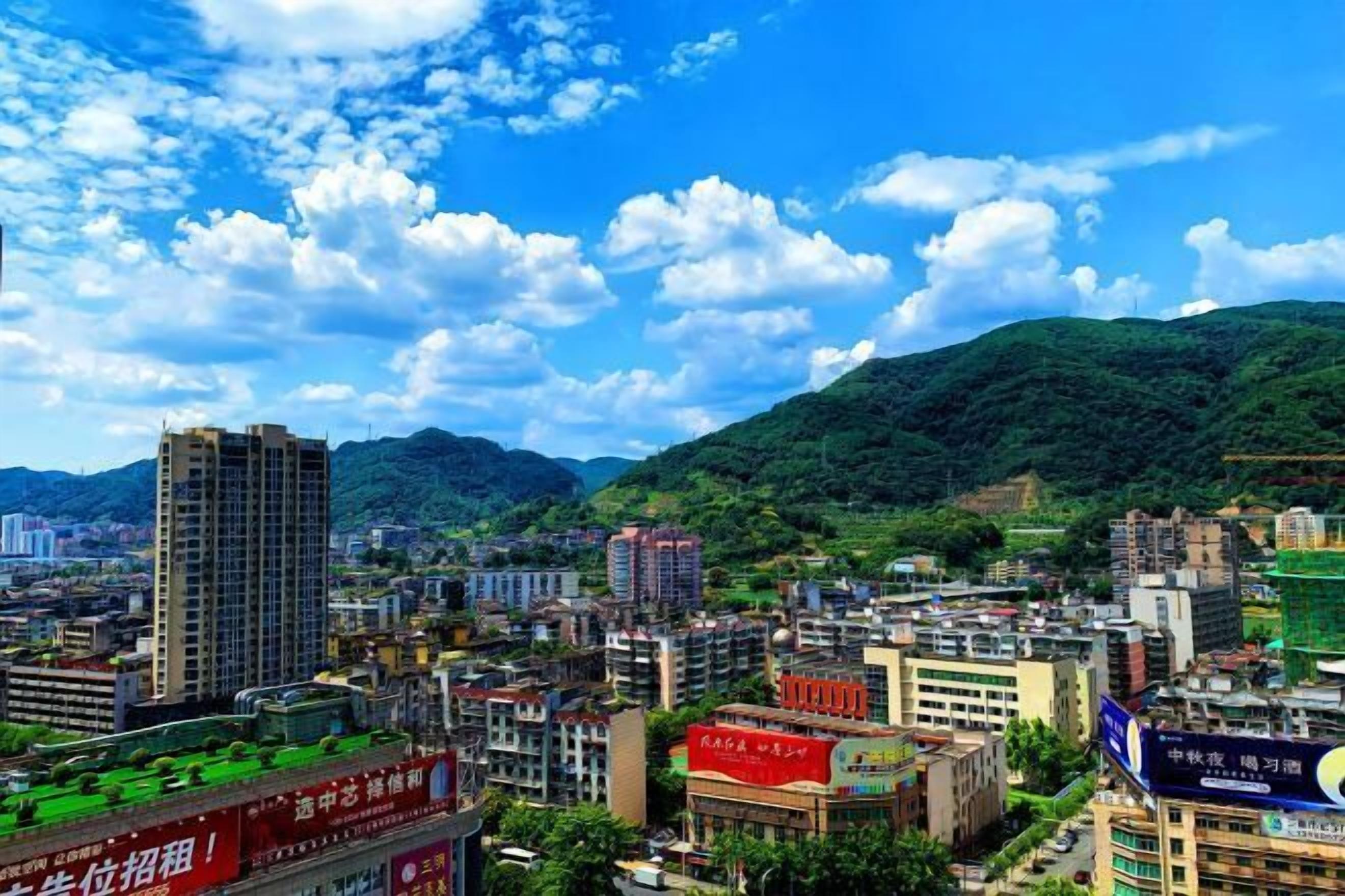 A cityscape with buildings, a prominent red sign, and a hill in the background.