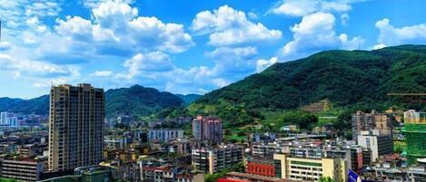 A cityscape with buildings, a prominent red sign, and a hill in the background.
