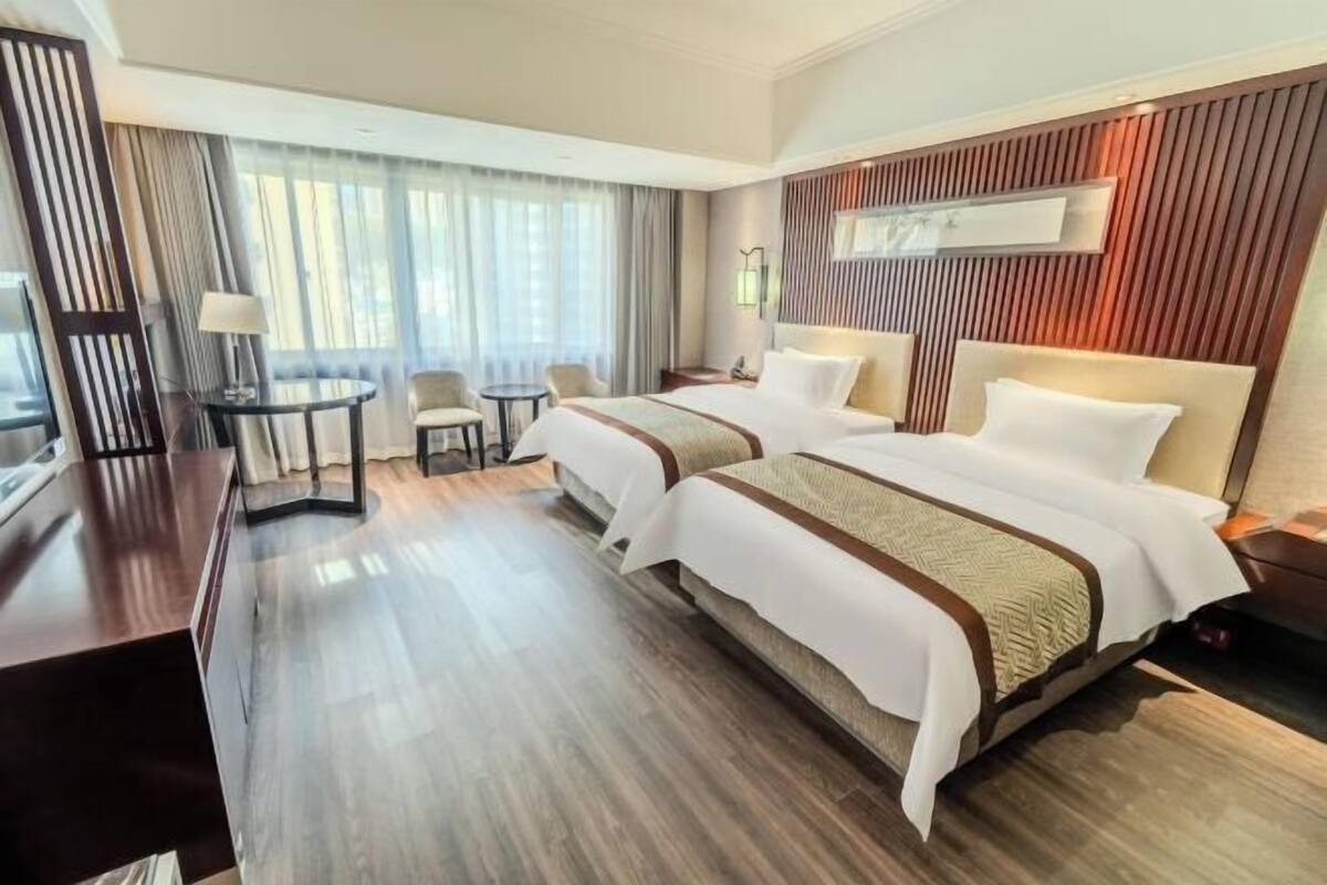 A hotel room with two beds, a desk, a chair, and a TV.