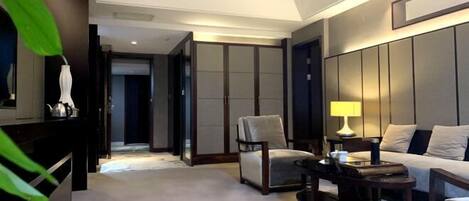 Habitación de hotel con sofá, sillón y una pequeña mesa. Se observa un armario con puertas correderas y una cama con cabecera.