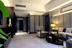 Habitación de hotel con sofá, sillón y una pequeña mesa. Se observa un armario con puertas correderas y una cama con cabecera.